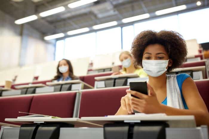 african student girl wearing face protective medical mask for protection from virus disease with smartphone at college lecture