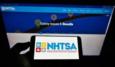 Person holding smartphone with logo of National Highway Traffic Safety Administration (NHTSA) on screen in front of website.