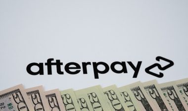 Dollar bills and blurrred Afterpay company logo seen paper background.