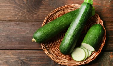 Fresh zucchini on wicker mat on wooden background