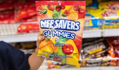 Child's hand holding a bag of Lifesavers brand gunnies candy in a supermarket aisle.
