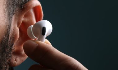 Close of man's ear showing his fingertips placing an Apple AirPod into his ear.