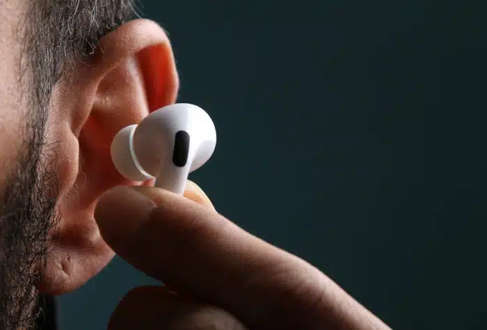 Close of man's ear showing his fingertips placing an Apple AirPod into his ear.