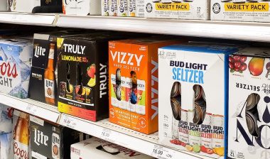 A view of several shelves filled with a variety of popular brands of hard seltzer beverages, on display at a local grocery store.