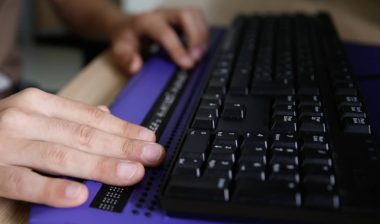Blind person using computer with braille computer display and a computer keyboard.