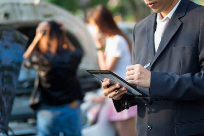 Side view of insurance agent writing on tablet while examining car after accident.