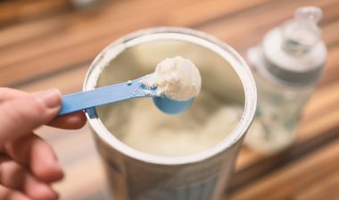 Powder milk and blue spoon on light background close-up.