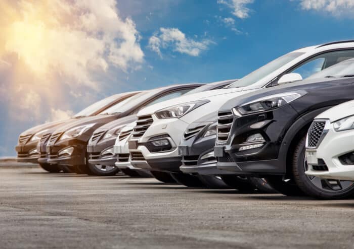 Cars in an auto sales lot row against a sunny blue sky - ford, nissan recall