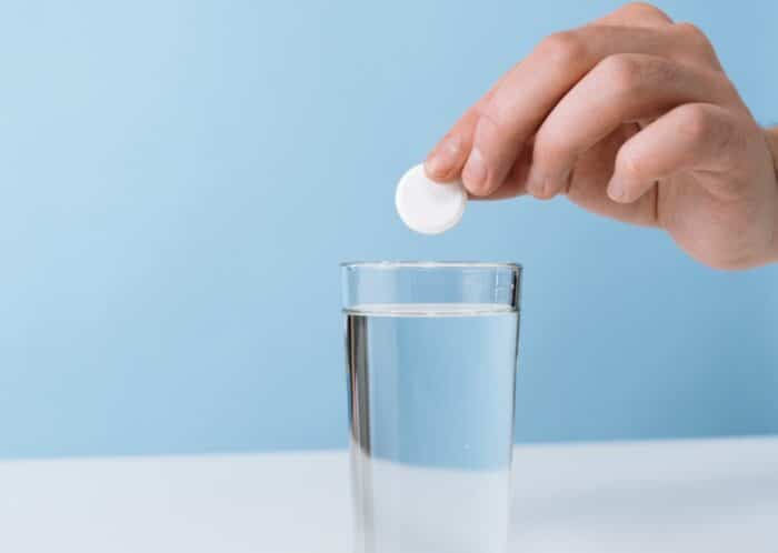 Close up of a persons hand dropping a effervescent tablet into a glass of water - Alka-Seltzer class action, non-drowsy