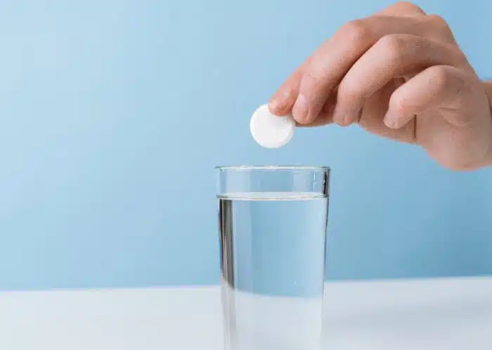 Close up of a persons hand dropping a effervescent tablet into a glass of water - Alka-Seltzer class action, non-drowsy