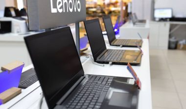 New Lenovo laptop computers are shown on retail display in electronic store. Brand logo in the background.