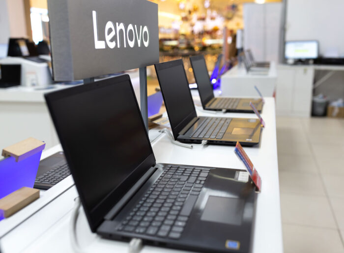 New Lenovo laptop computers are shown on retail display in electronic store. Brand logo in the background.