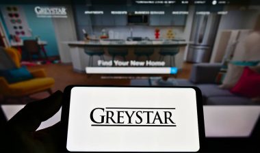 Person holding mobile phone with logo of Real estate company Greystar Real Estate Partners LLC on screen in front of website.