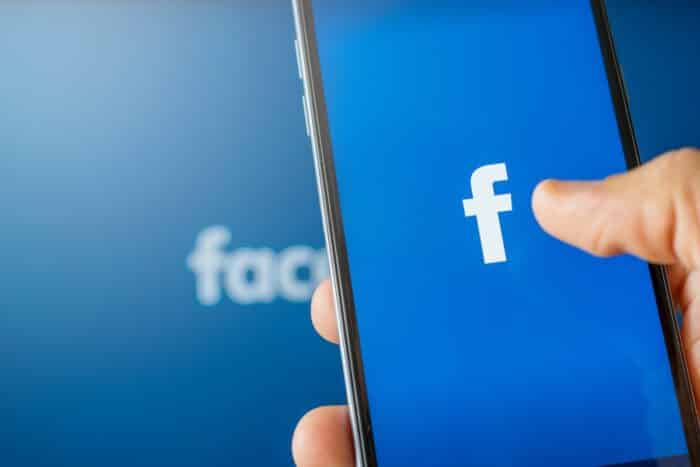 Phone showing facebook app on the screen. Facebook is a photo sharing social media desktop background - meta class action, youth, mental health