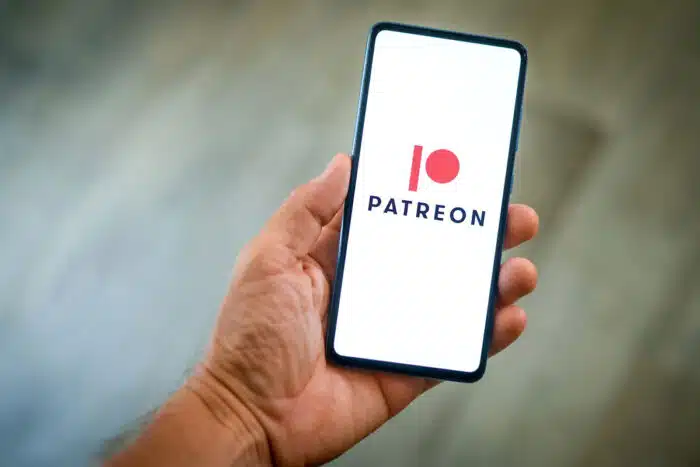 Close up view of hand with smartphone and Patreon logo on display - facebook