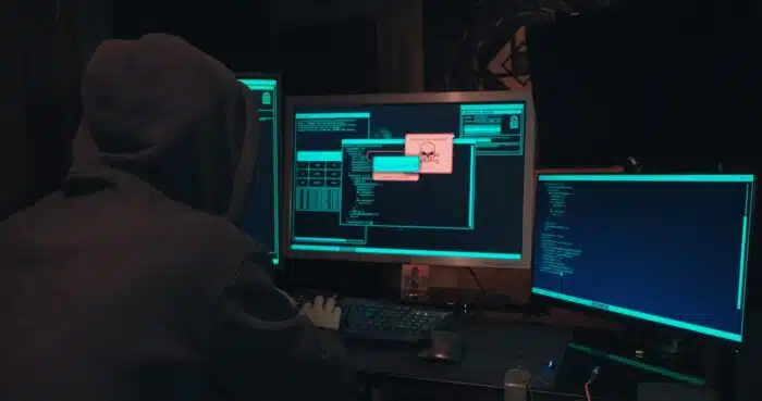 Hacker in a hood sits in front of computer screens and hacks databases - river city bank lawsuit
