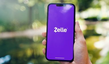 Girl in the park holding a smartphone with Zelle instant payment system app on the screen.