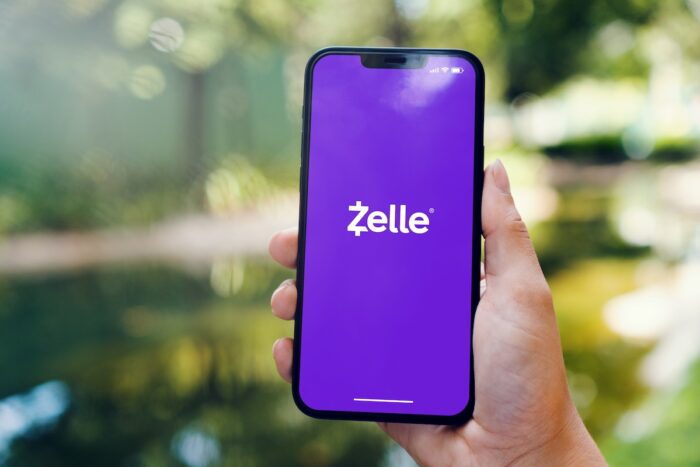 Girl in the park holding a smartphone with Zelle instant payment system app on the screen.