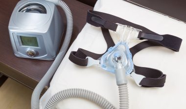 Sleep apnea CPAP headgear mask and hose on white pillow attaching to CPAP machine, for people with sleep apnea or sleep disorder.