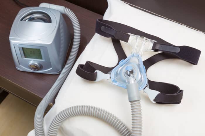 Sleep apnea CPAP headgear mask and hose on white pillow attaching to CPAP machine, for people with sleep apnea or sleep disorder.