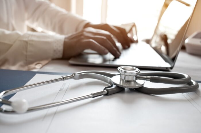 Doctor's working on laptop computer, writing prescription clipboard with record information paper folders on desk in hospital or clinic - San Diego Family Care data breach