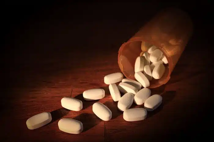 Opioid capsules spill from a bottle on a wooden table with dramatic light