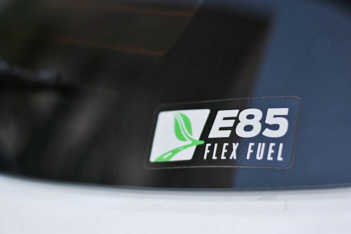 Soft focus image of sticker with logo and text “E85 FLEX FUEL" holding onto rear window of a car. 
