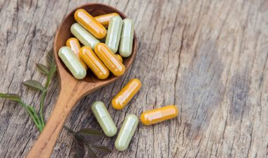 Various laxative capsules on a wooden spoon against a wood background.