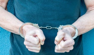 torso view of Caucasian man with hands in handcuffs against a black shirt