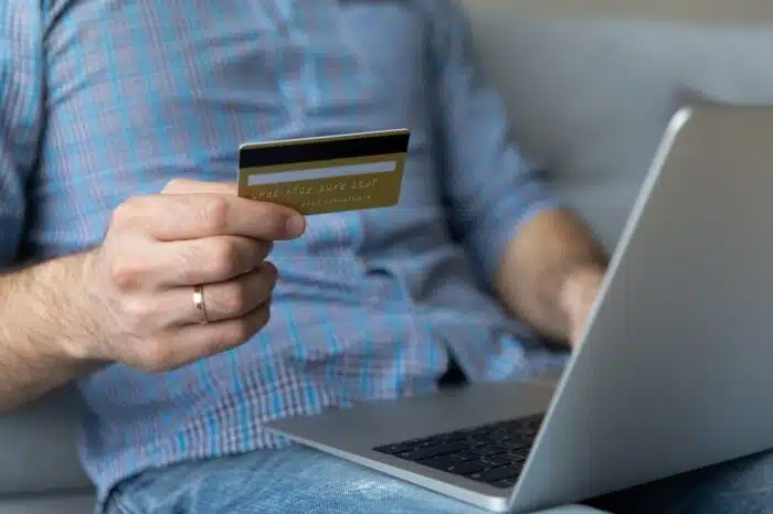 Cropped close up image man sit on sofa with laptop holds credit card buying on internet