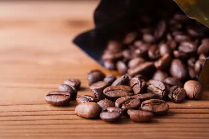 Close up of coffee beans spilling out of a bag onto a wood surface - kona coffee settlement, hikc, kroger