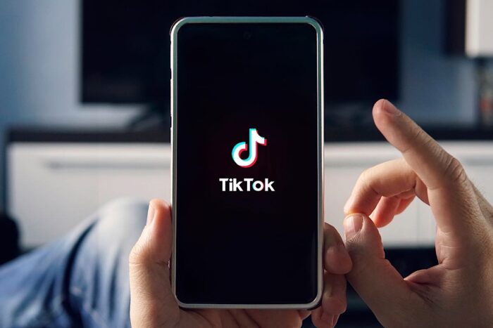 Man holding smartphone with TikTok logo on screen - meta 