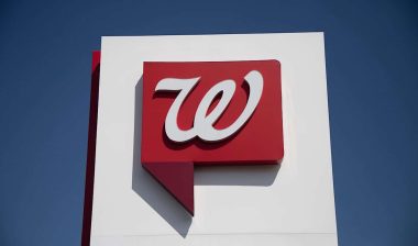 Close up of Walgreens logo signage against a blue sky.