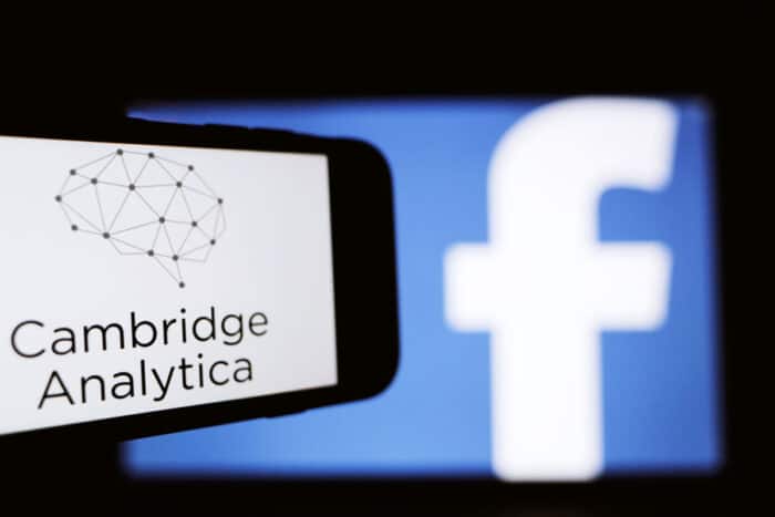 The logo of the strategic communication company Cambridge Analytica is seen on the screen of an iPhone in front of a computer screen showing Facebook logo.