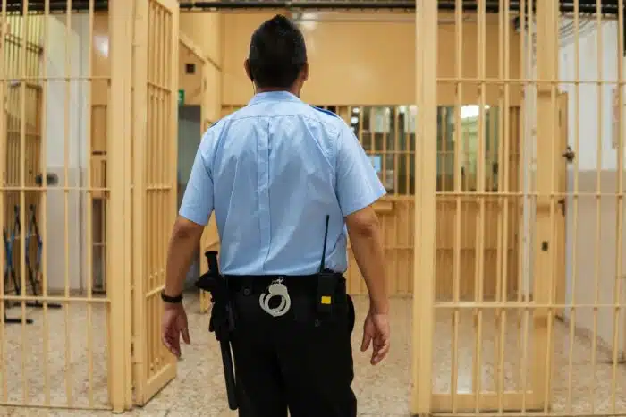 A corrections officer in a blue shirt, dark pants, and utility belt is seen from the back walking through a prison cell door - mdoc settlement, mdoc class action lawsuit