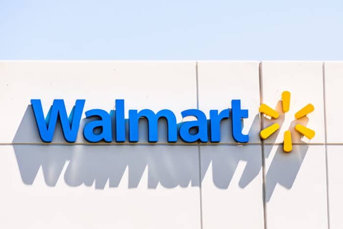 Close up of Walmart sign displayed on exterior of building against a blue sky.
