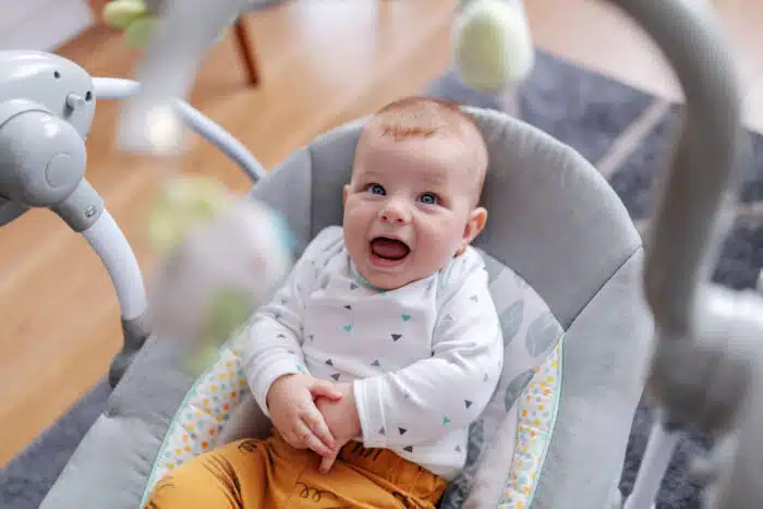 6 months old baby boy sitting in his rocker chair, talking baby language and looking at toys.