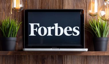 Close up of Forbes logo displayed on a laptop screen against a wood wall.