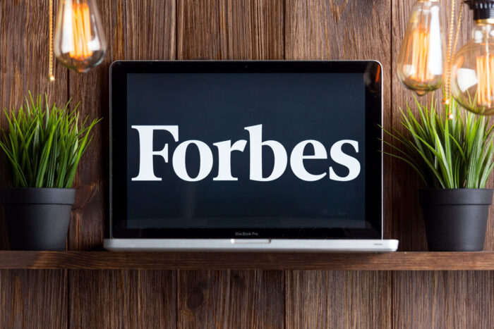 Close up of Forbes logo displayed on a laptop screen against a wood wall.