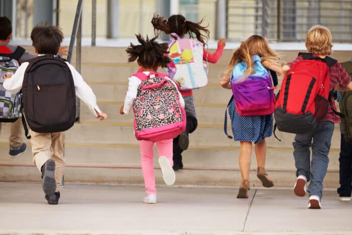 Elementary school kids running into school, back view.