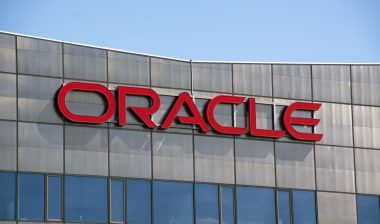 Close up of Oracle signage on exterior of a building against a blue sky.