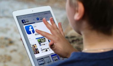 Boy teenager installs a program of the social network Facebook on iPad Air Apple from iTunes.