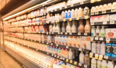 Defocused blurred selection of dairy products in open front cold fridge at retail store in USA.