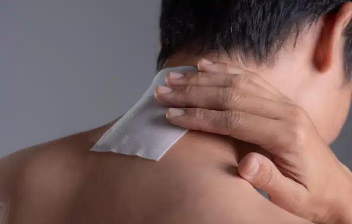 Close up of a lidocaine patch on the back of a man’s neck.