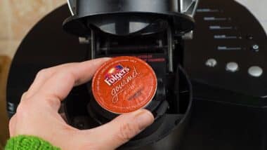 Close-up of woman inserting single-serve K-cup Foldger's coffee into a Keurig coffee maker.