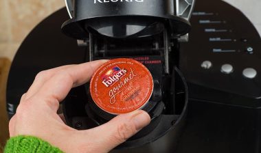 Close-up of woman inserting single-serve K-cup Foldger's coffee into a Keurig coffee maker.