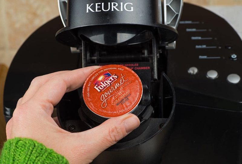 Close-up of woman inserting single-serve K-cup Foldger's coffee into a Keurig coffee maker.