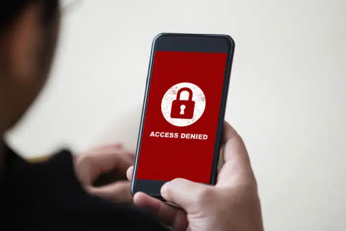 Man holding smartphone with access denied text on screen.