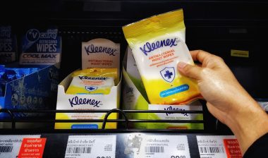 Man's hands are holding wet tissue (Brand "Kleenex") stacked on a shelf in a supermarket.