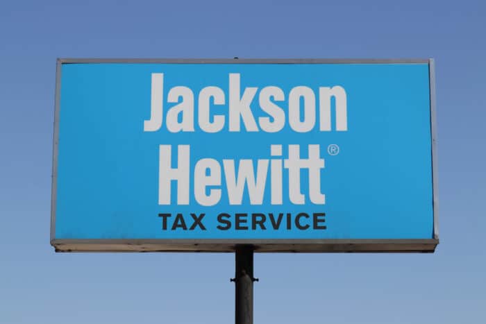 Close up of Jackson Hewitt on a billboard sign against a blue sky.